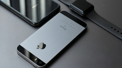 Two iPhones face down on a dark surface beside a black smartwatch. The sleek devices convey a modern and minimalist aesthetic.