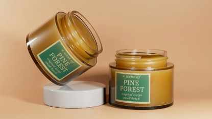 Two amber jars labeled "Pine Forest" on a peach background; one closed and tilted, the other open. They evoke a natural and calming atmosphere.