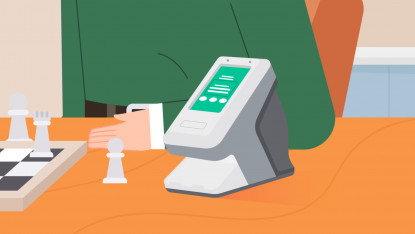 A person in a green sweater and orange chair sits at a table with a chessboard and a digital payment terminal. The scene conveys focus and concentration.
