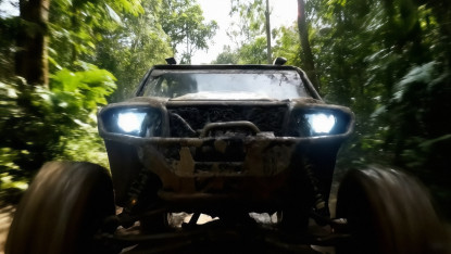 A rugged off-road vehicle with bright headlights navigates through a dense, lush forest. The scene conveys an adventurous and exhilarating mood.