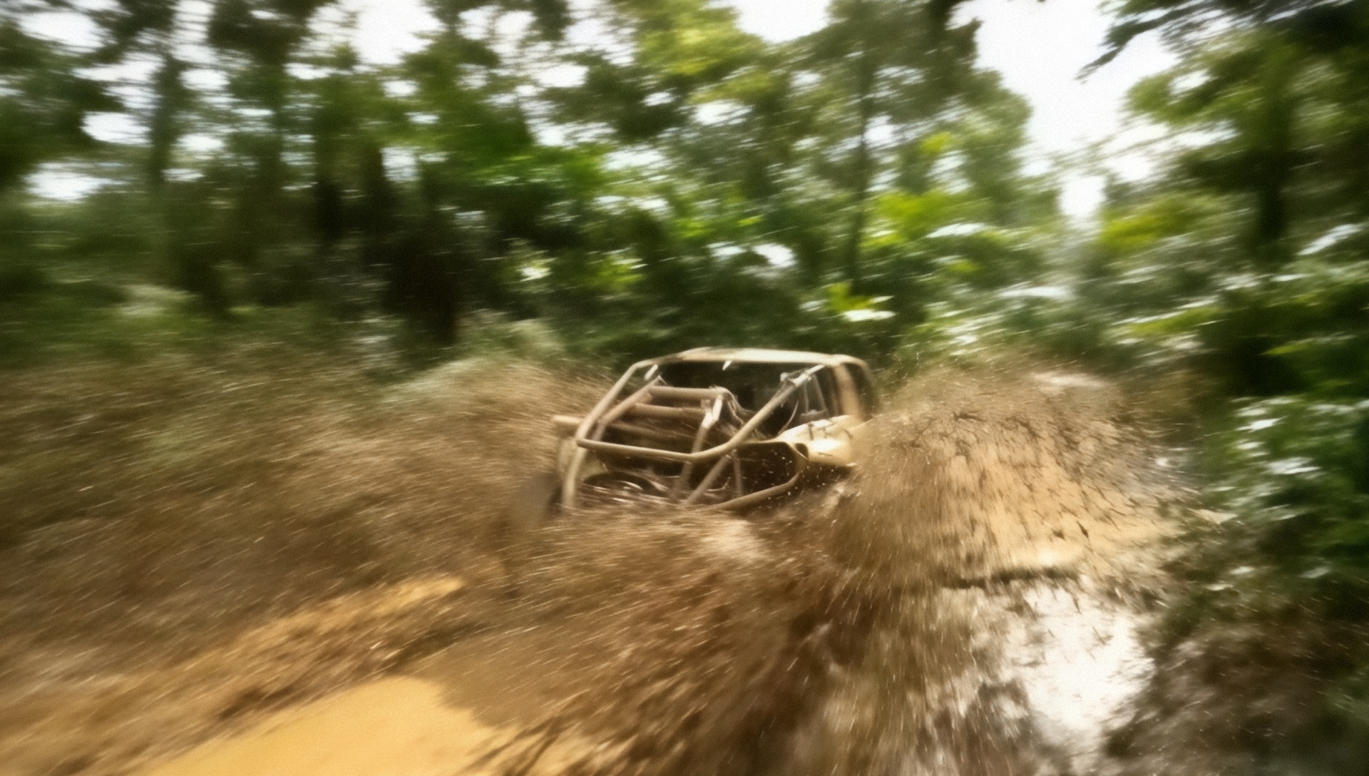 A rugged off-road vehicle speeds through a muddy trail, flinging dirt in all directions. Surrounded by dense, green forest, the image conveys excitement and adventure.