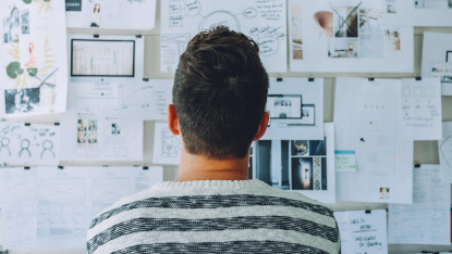 A person in a striped sweater faces a wall covered with various sketches and notes, suggesting creativity and brainstorming in a design process.