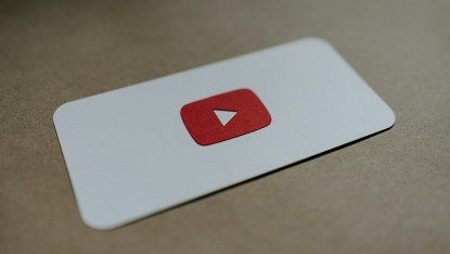 A small white card displays a red YouTube logo with a white play button, placed on a brown surface. The image conveys a sense of modern digital media.